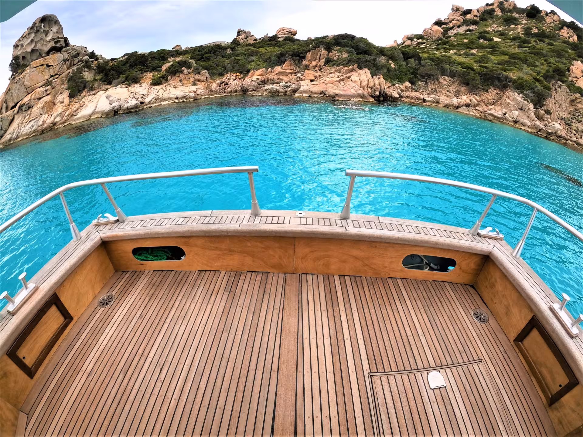 View from a boat deck overlooking the turquoise waters of La Maddalena Archipelago, featuring rocky coastline.