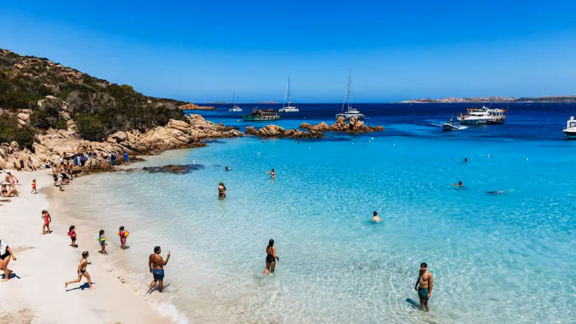 Tourists enjoying a sunny day on a pristine beach with crystal-clear waters in La Maddalena Archipelago.