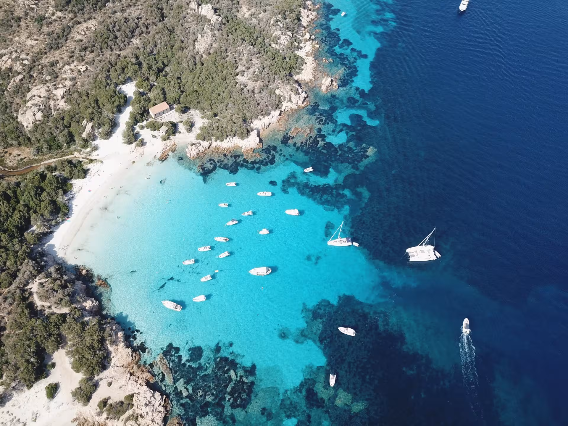 Aerial view of boats in the turquoise waters of La Maddalena Archipelago, showcasing stunning coastline and clear seas.