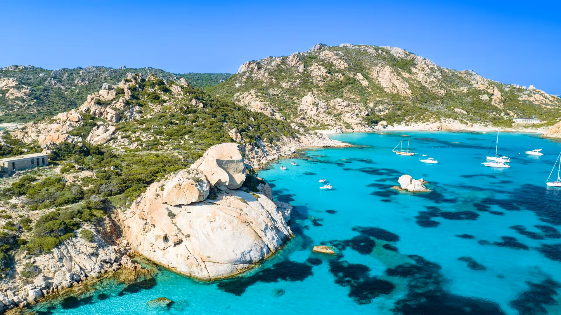 Breathtaking landscape of La Maddalena Archipelago with boats anchored near rocky coastal hills.