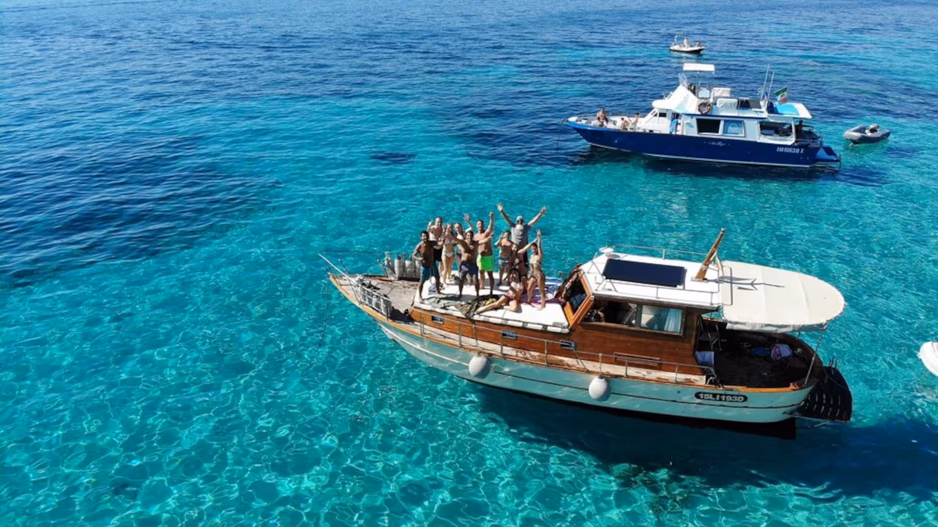 Group enjoying a sunny day on a wooden boat tour in La Maddalena Archipelago, surrounded by turquoise waters.