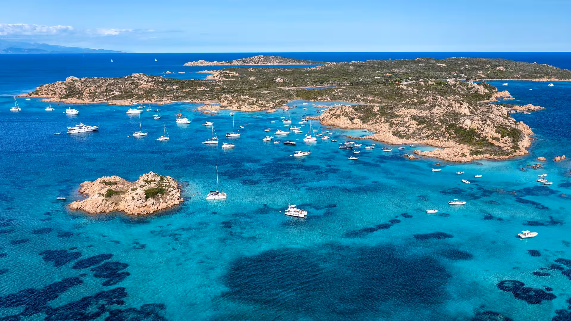Aerial view of yachts scattered across the vibrant blue waters of La Maddalena Archipelago.