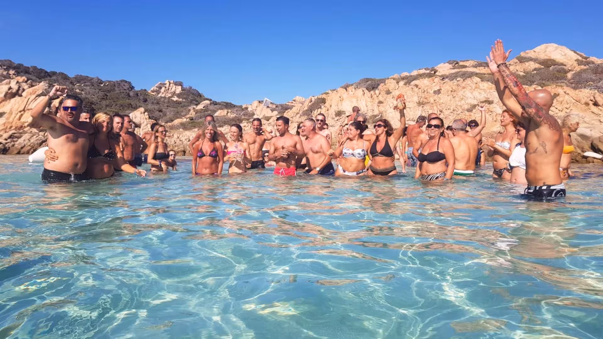 Group of joyful tourists enjoying crystal-clear waters on a La Maddalena Archipelago catamaran tour from Cannigione.