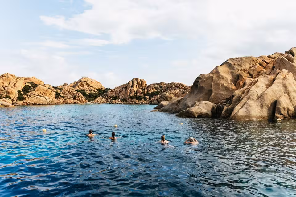 Swimmers enjoy the crystal-clear waters and dramatic rock formations of La Maddalena Archipelago on a sunny day.