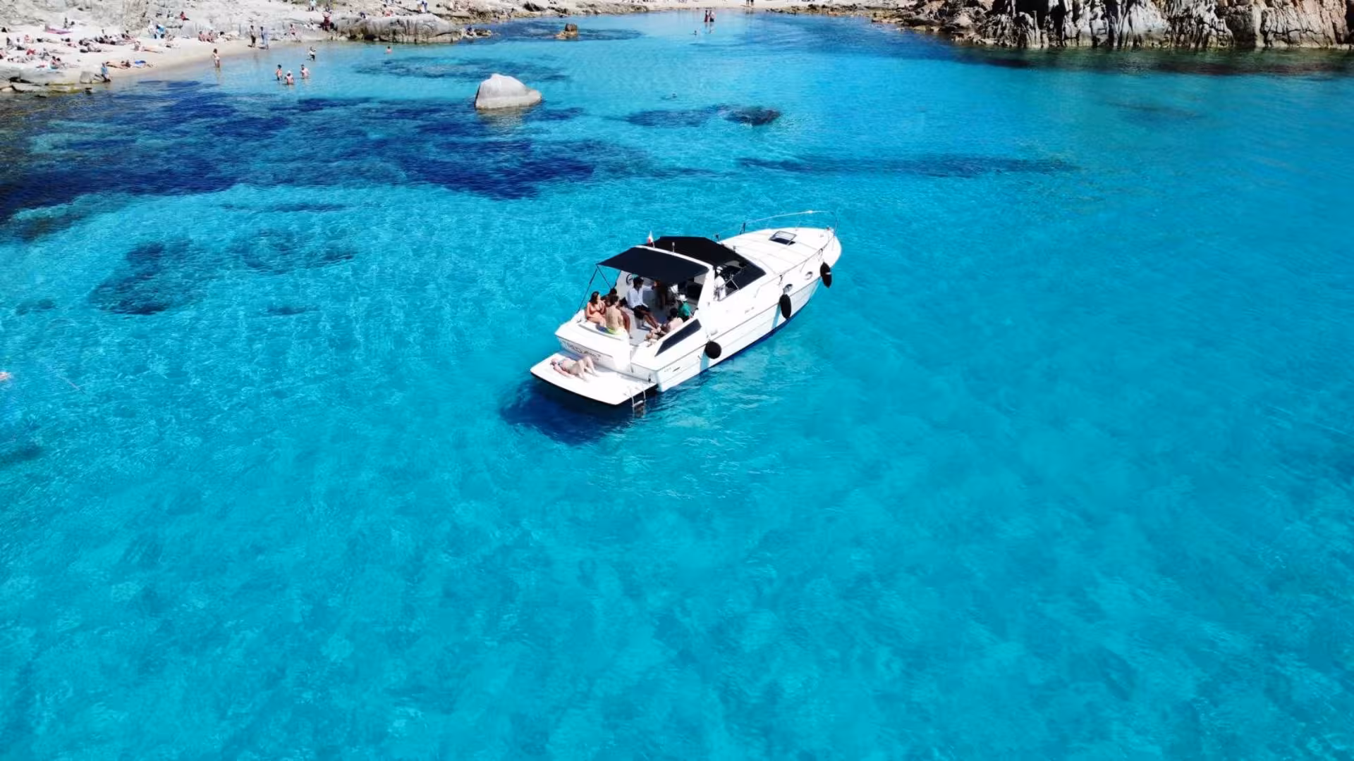 Aerial view of a boat tour in La Maddalena Archipelago, surrounded by crystal-clear turquoise waters and sunbathers.