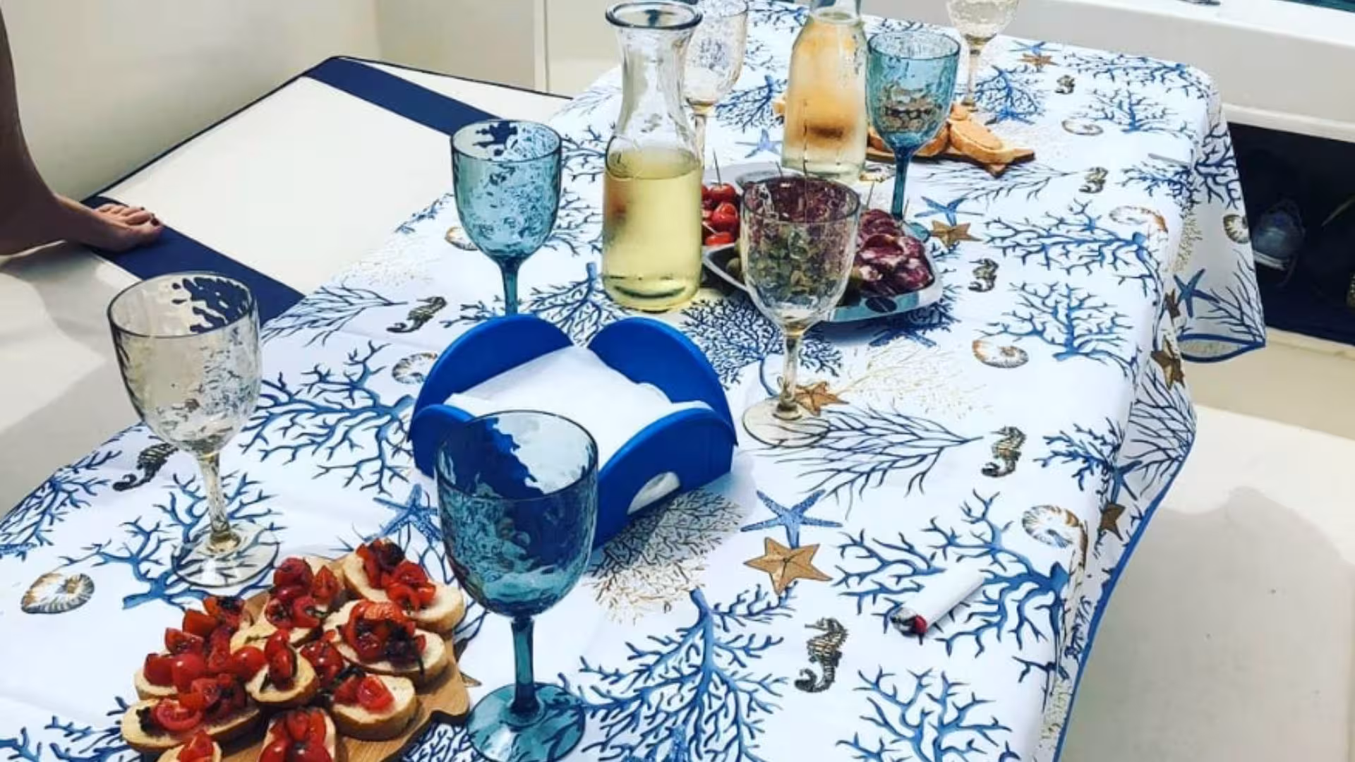 Gourmet snacks and wine set on a nautical-themed tablecloth during a boat tour in La Maddalena Archipelago.