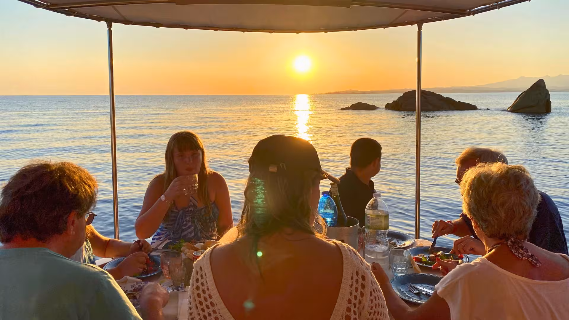 Group dining on a boat during a stunning sunset in La Maddalena Archipelago, perfect for a private tour experience.