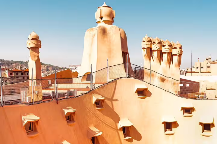 Rooftop view of La Pedrera showcasing whimsical chimneys and undulating forms against a clear sky.