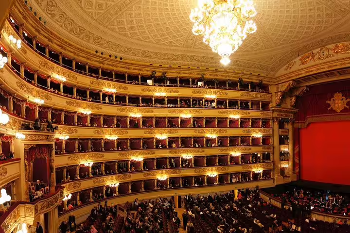 Opulent interior of La Scala Theatre in Milan with golden balconies, red velvet seats and guests arriving for a private guided tour