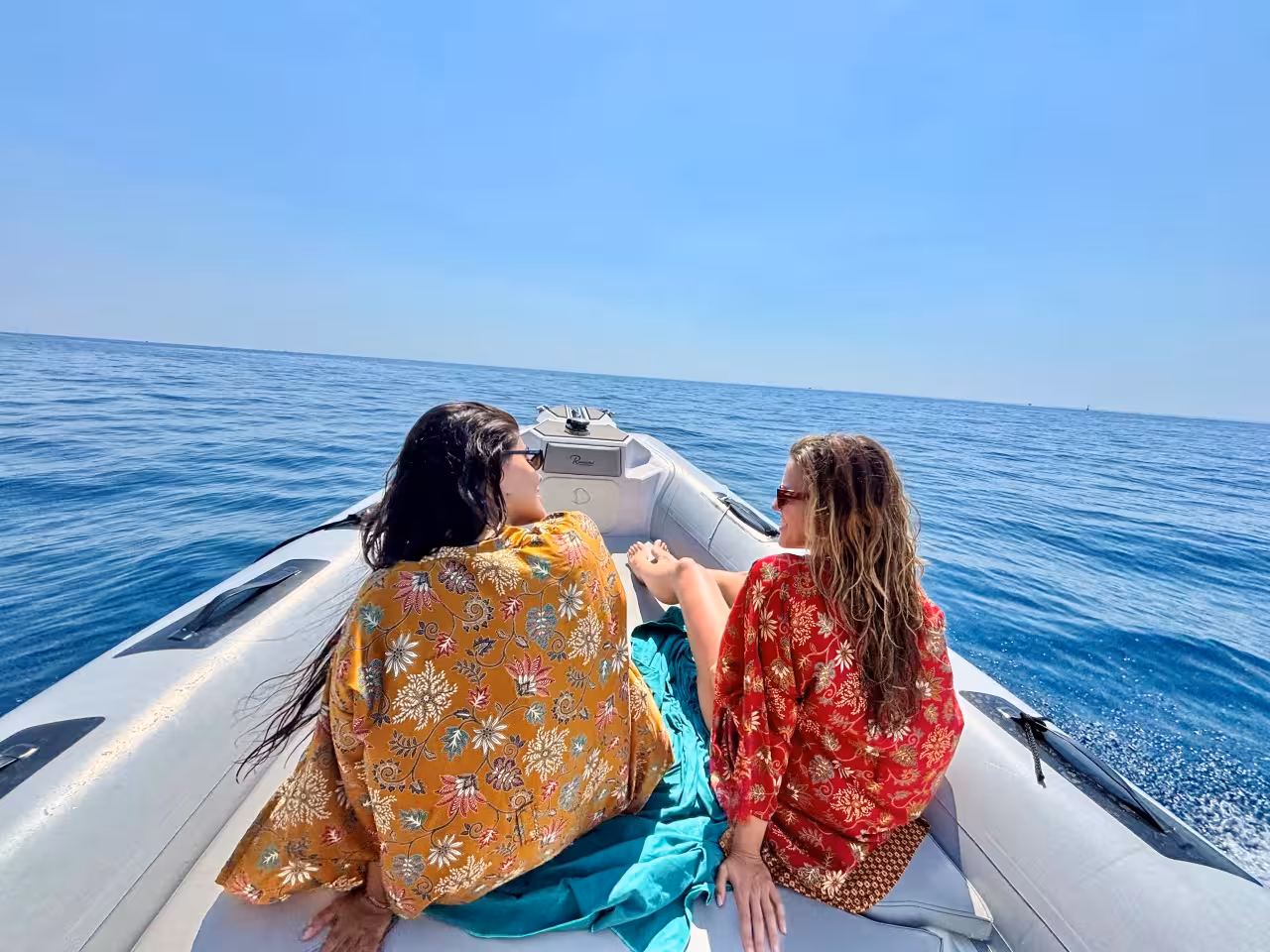 Two women sunbathe on a speedboat cruising the Ligurian Sea on a La Spezia Cinque Terre full-day boat tour
