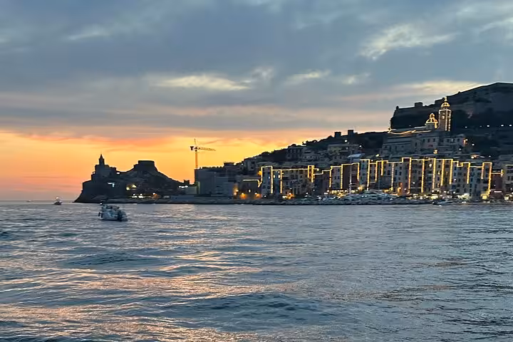 Sunset view of Portovenere with illuminated buildings along the coast, perfect for a La Spezia boat tour.