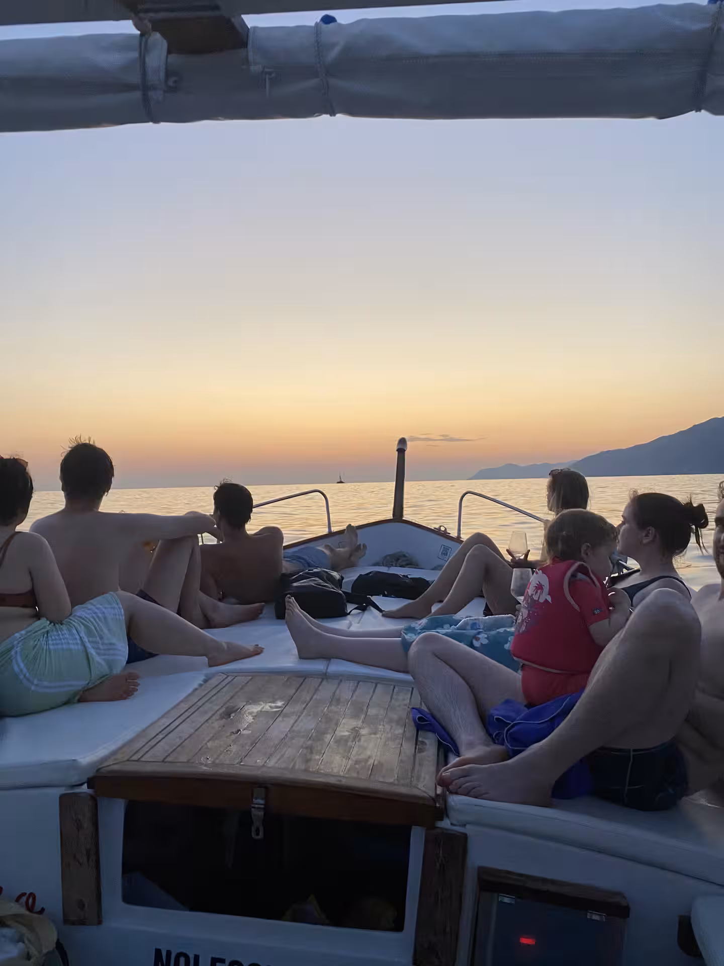 Group of people enjoying a sunset boat tour in Golfo Dei Poeti, La Spezia, relaxing on deck with coastal views.