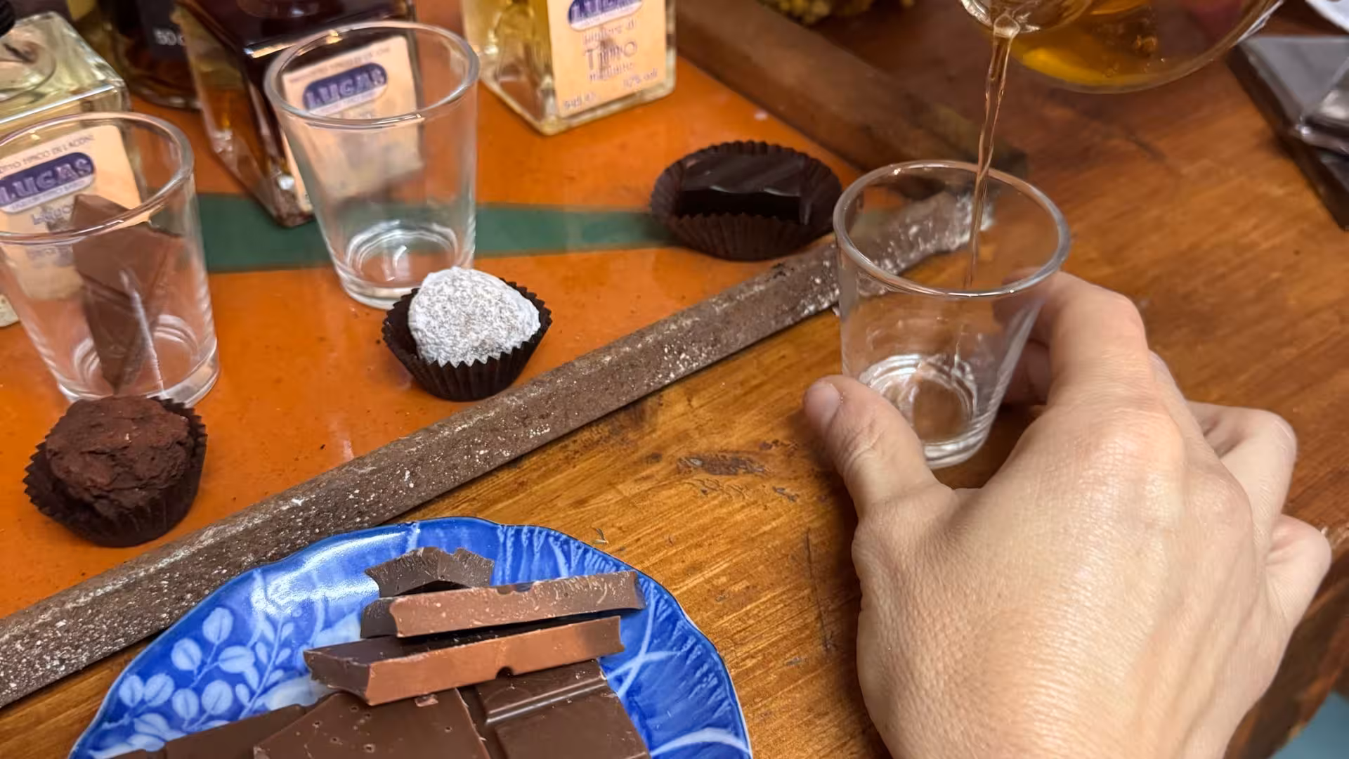 Hand pouring local liqueur into a glass alongside assorted chocolates for Laconi tasting experience.