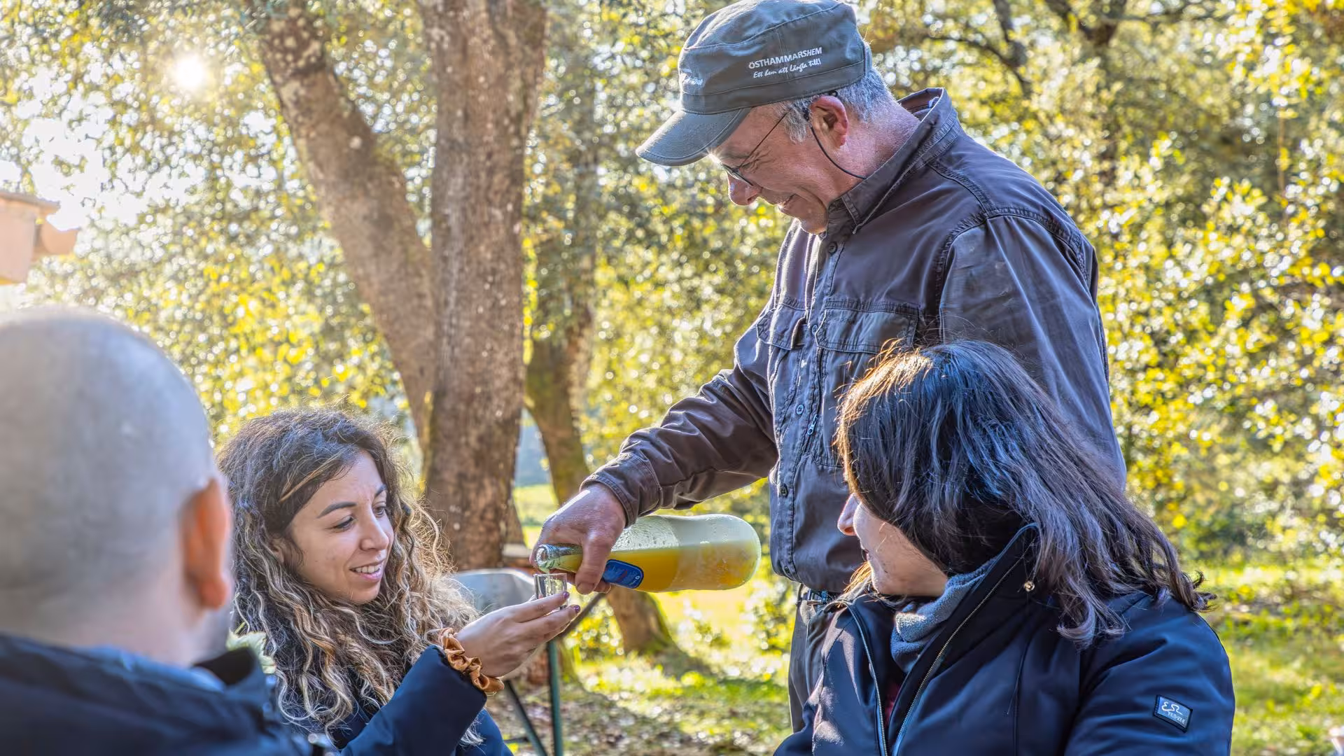Man serving a refreshing aperitif to truffle hunting participants in a sun-dappled forest setting in Laconi.