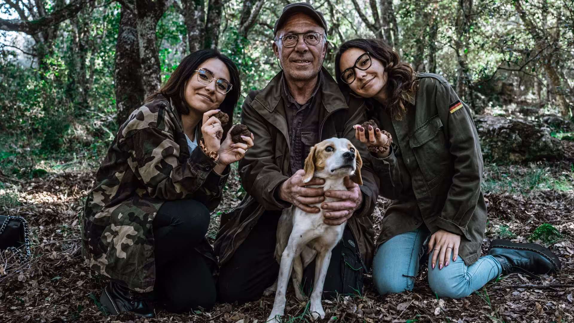 Happy group with truffles and dog during Laconi truffle hunting tour in a lush forest setting.