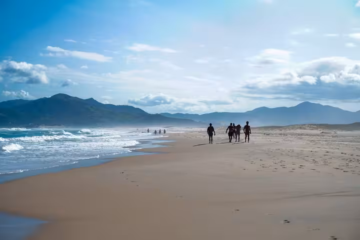 Visitors strolling along the pristine beach of Lagoinha do Leste, with scenic mountains in the background.