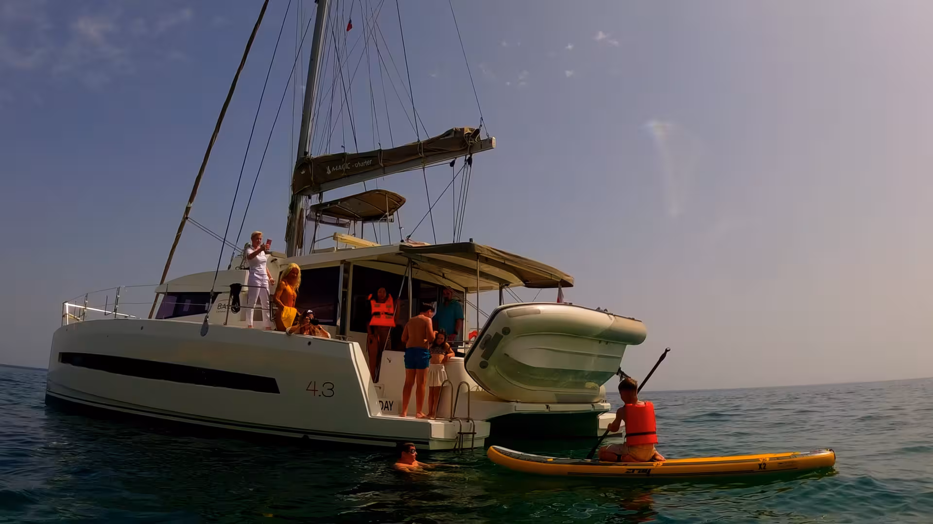 Guests swimming and paddleboarding beside catamaran at sea, Lagos full-day catamaran cruise adventure Algarve