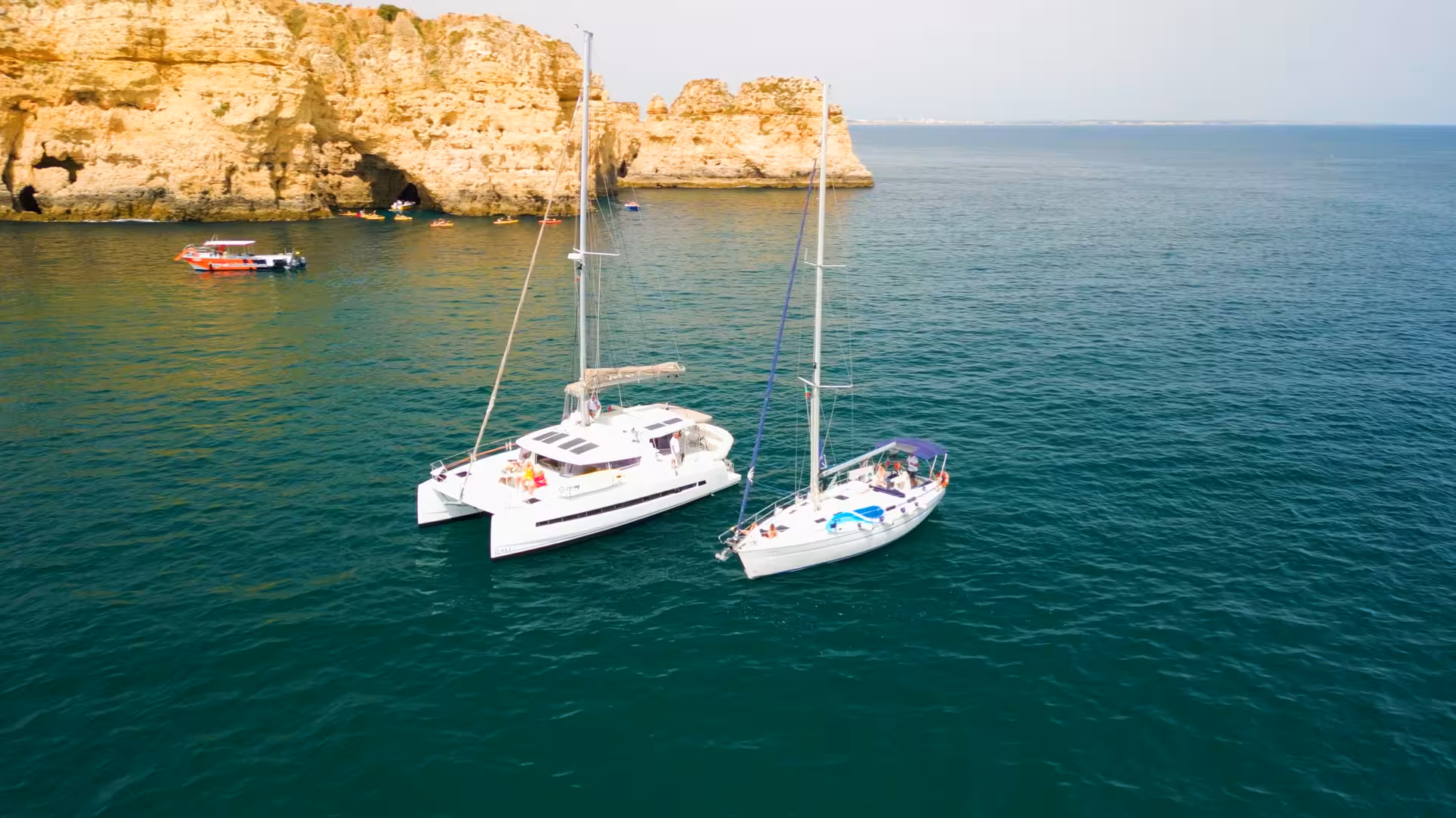 Aerial view of Lagos catamaran sailing near Algarve sea cliffs, scenic daytime cruise on turquoise water