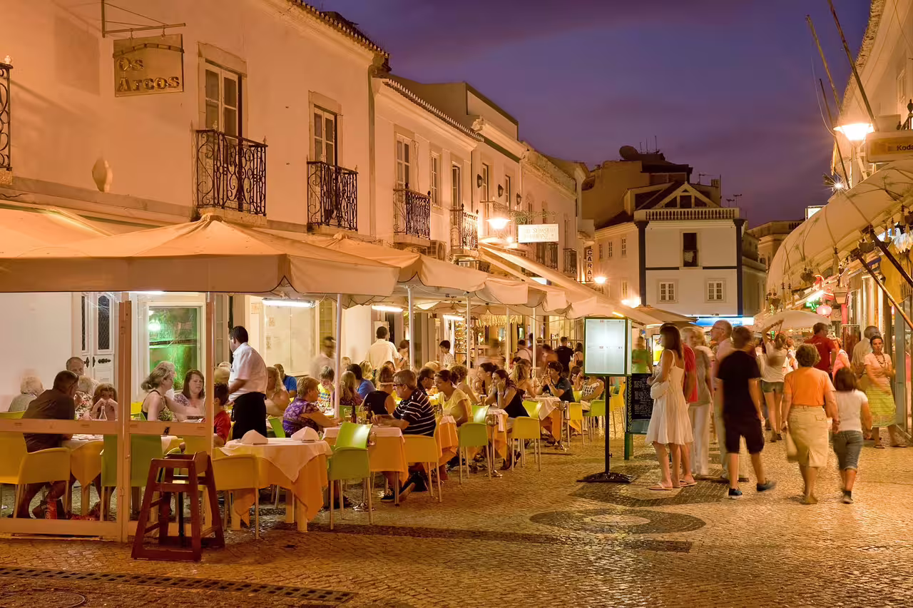 Nightlife in Lagos, Portugal: bustling street with outdoor dining, vibrant atmosphere, perfect for a private Benagil tour experience.