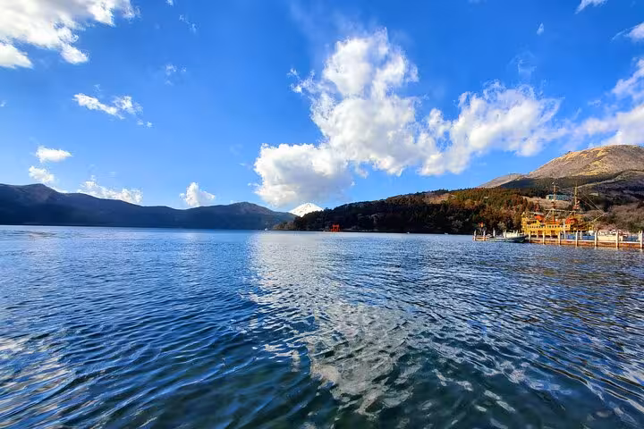 Expansive view of Lake Ashi under a bright blue sky with distant mountains and a pirate ship in Hakone.
