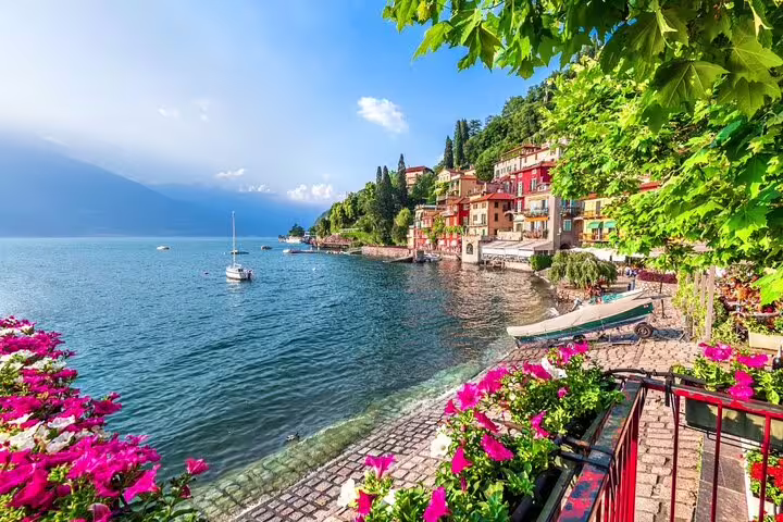 Charming lakeside path adorned with flowers and colorful buildings along Lake Como, inviting private exploration.