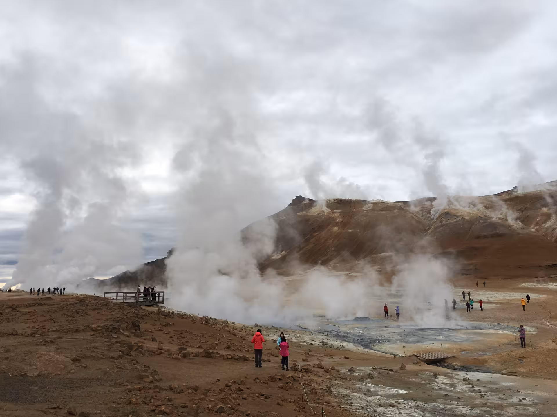 Tourists exploring the steaming geothermal area near Lake Myvatn with a backdrop of barren, rocky terrain.