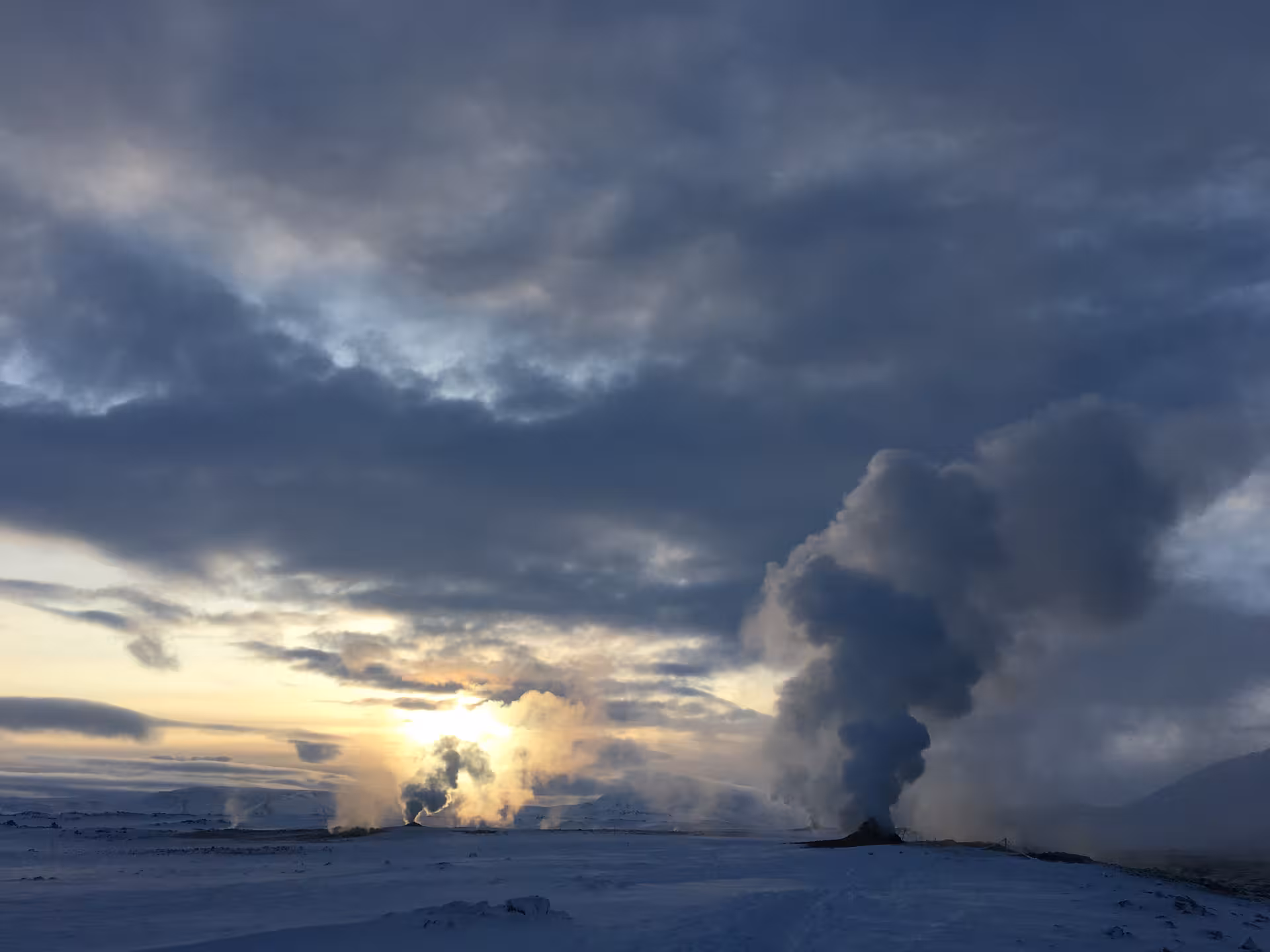 Dramatic sunset over snowy geothermal fields near Lake Myvatn with steam rising under a cloudy sky.