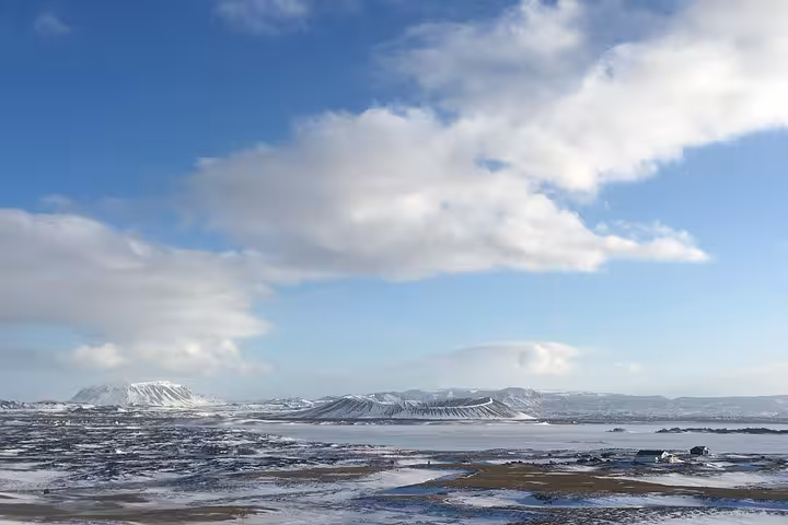 Stunning panoramic winter view of Lake Myvatn surrounded by snow-capped mountains under a bright blue sky.