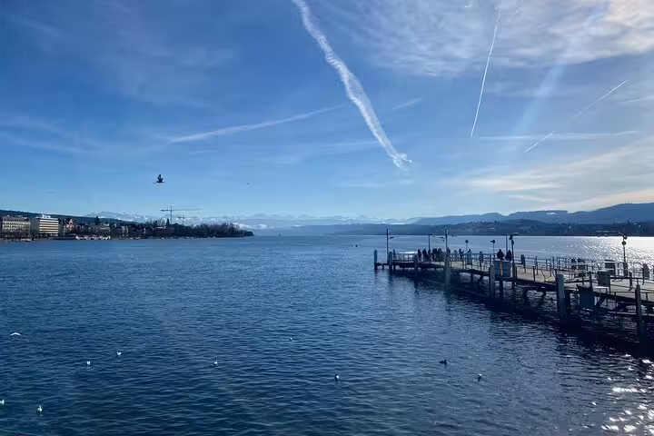 Serene view of Lake Zurich with a pier and distant mountains, perfect for a relaxing cruise on a sunny day.