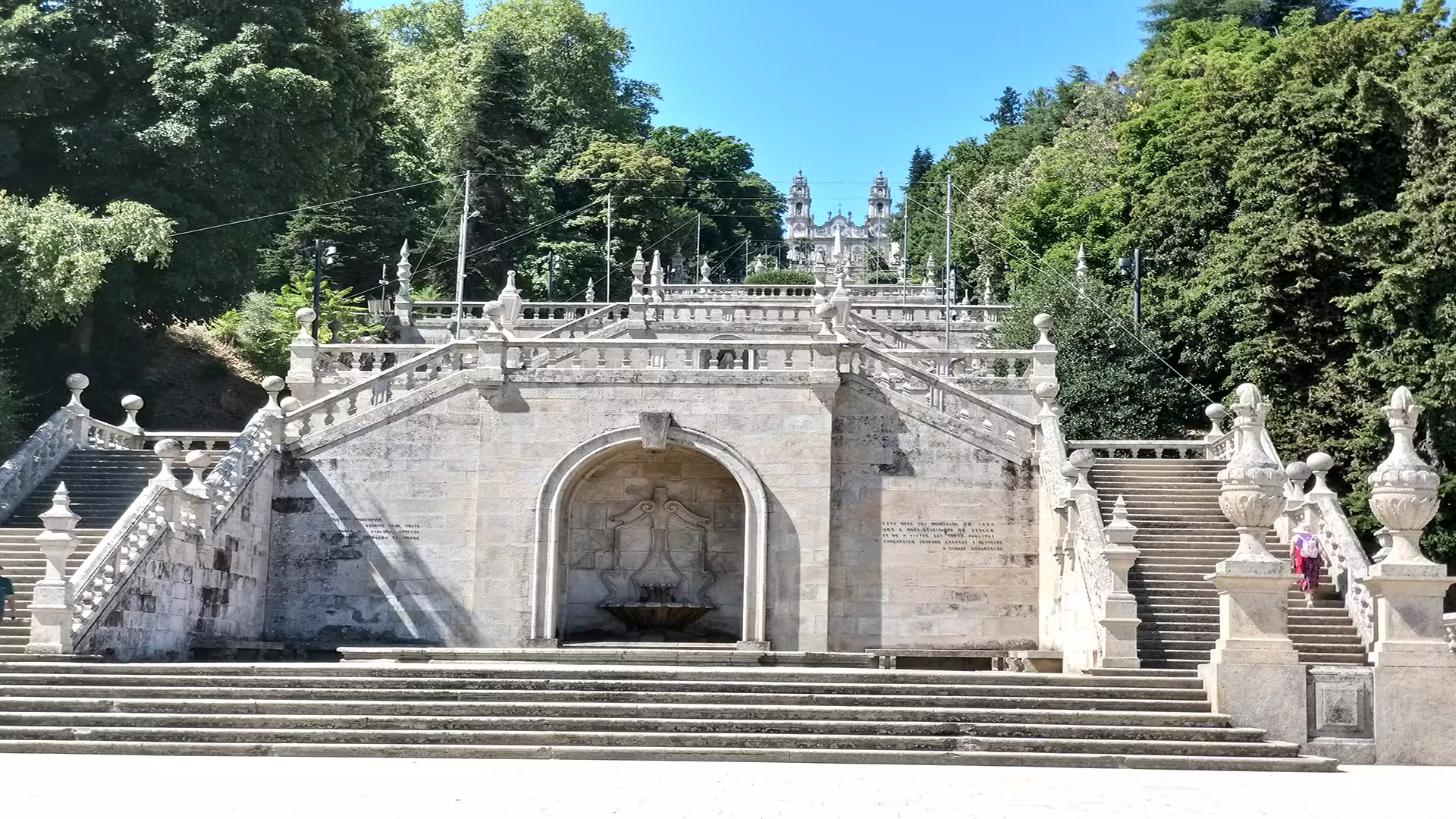 Baroque staircase of Sanctuary of Nossa Senhora dos Remédios in Lamego, Portugal, surrounded by lush greenery.