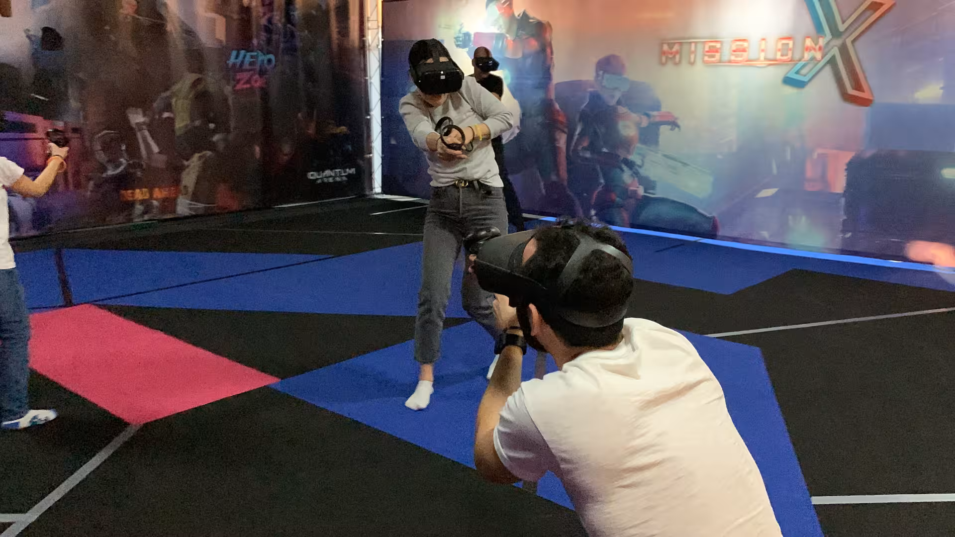 Players dueling in Laser Game VR 25 arena, aiming VR blasters with headsets on a colorful mission set