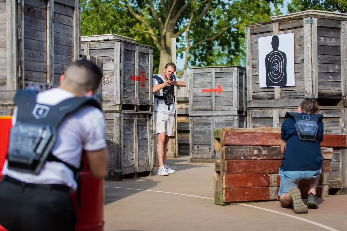 Players in vests aiming in an outdoor laser tag arena in Amsterdam, using wooden cover for team battles