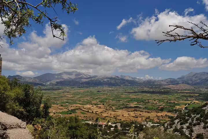 Panoramic view of the lush Lasithi Plateau with distant mountains under a partly cloudy sky, Crete.