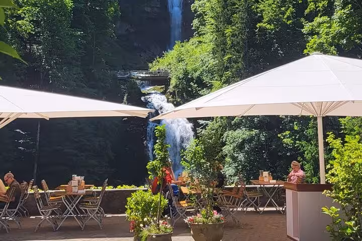 Scenic outdoor cafe with umbrellas near a waterfall in the lush Swiss Alps, perfect for a private tour in Lauterbrunnen.