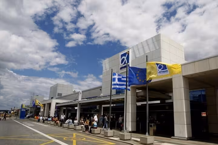Athens Airport terminal entrance with Greek flags, drop-off point for Lavrio Port to ATH private transfer