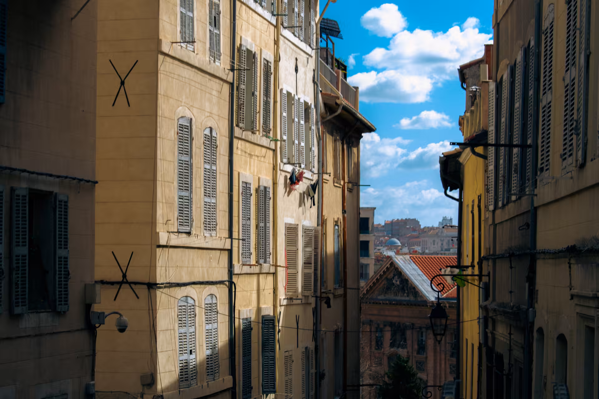 Sunlit Le Panier street in Marseille with shuttered facades and Old Port skyline on a guided walking tour