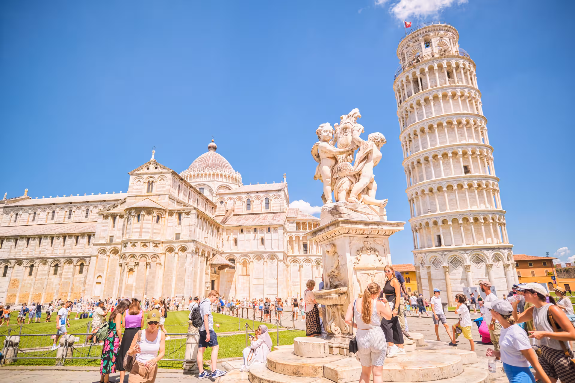Tourists exploring the iconic Leaning Tower of Pisa and the intricate Pisa Cathedral under a clear blue sky.