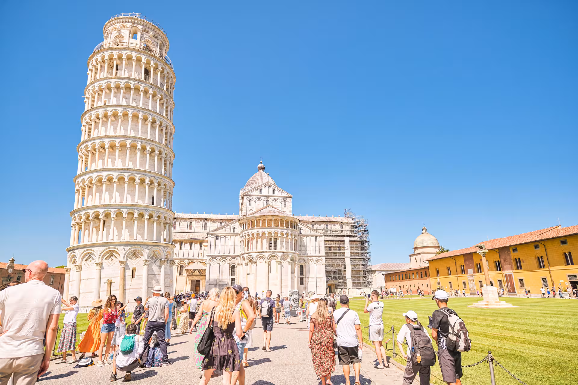 Tourists admire the Leaning Tower of Pisa and Pisa Cathedral under a clear blue sky during the half-day tour.