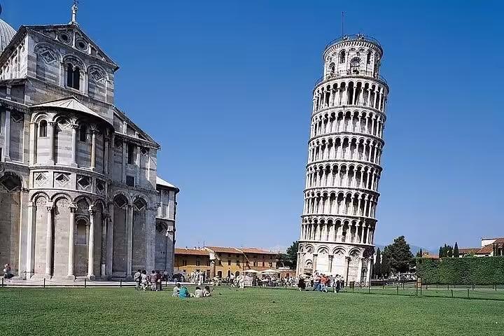 Famous Leaning Tower of Pisa and Pisa Cathedral under a bright blue sky, surrounded by lush green lawn.