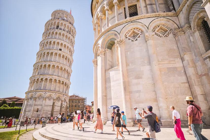Tourists explore the iconic Leaning Tower of Pisa and nearby cathedral in Piazza dei Miracoli on a sunny day.
