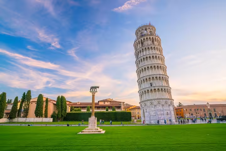 Iconic Leaning Tower of Pisa against a vibrant sunset sky surrounded by lush green lawns.