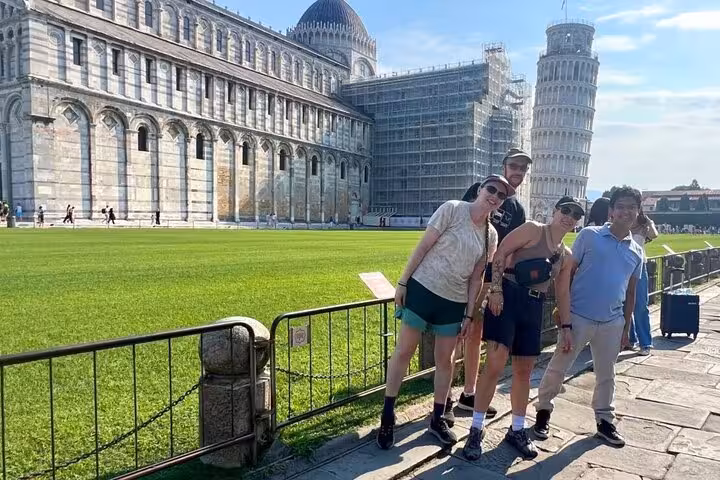 Tourists posing playfully near the Leaning Tower of Pisa on a sunny day.