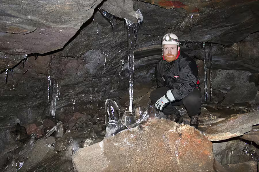 Explorer in Leidarendi Lava Tunnel, Iceland, surrounded by icy formations, showcasing small group caving adventure.