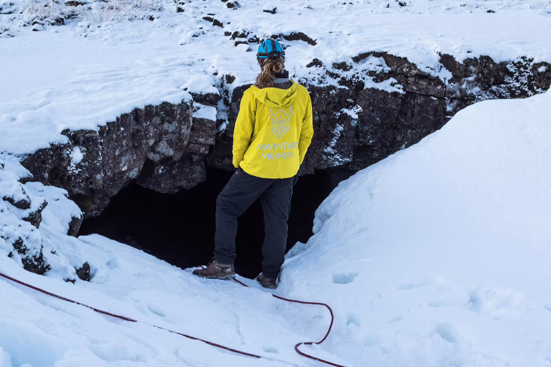 Adventurer in yellow jacket stands at snow-covered entrance of Leidarendi Lava Tunnel, ready for a small group caving tour.
