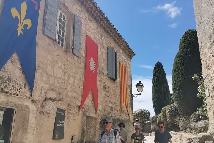 Walking tour in Les Baux-de-Provence medieval street with stone houses, banners and cypress views