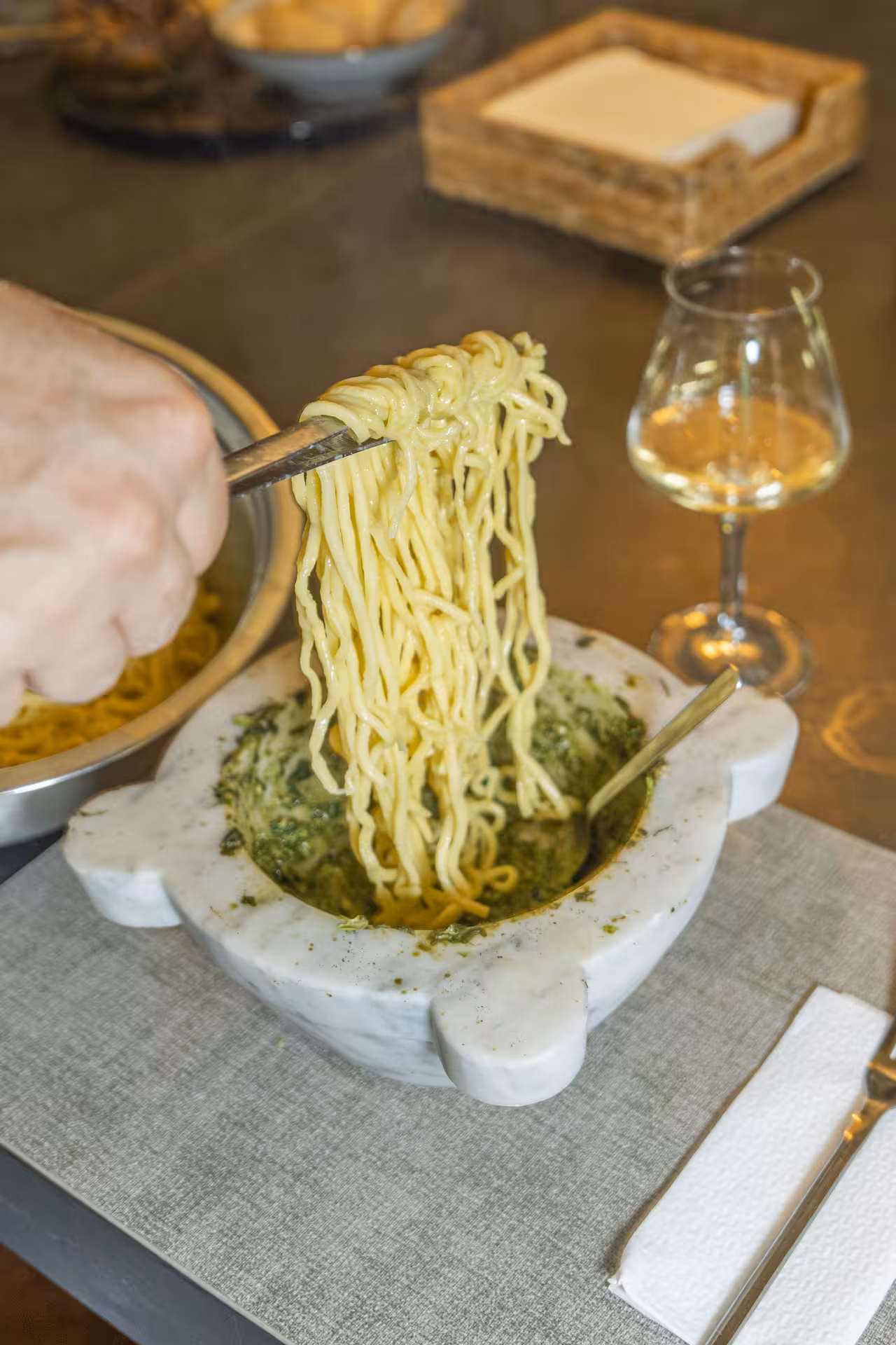 Freshly made pasta being mixed with pesto in a mortar, paired with a glass of white wine in a Ligurian cooking class.