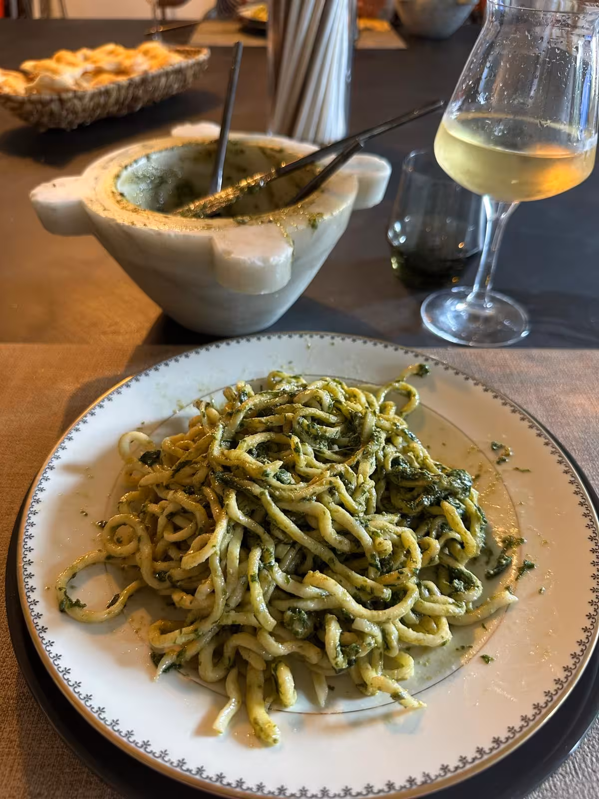 Plate of fresh pasta with pesto, accompanied by wine and a mortar, highlighting Ligurian culinary delights.