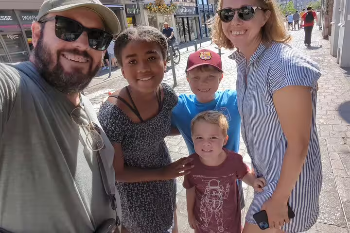 Family selfie on a sunny Lille street during a scavenger hunt walking tour, exploring city highlights together