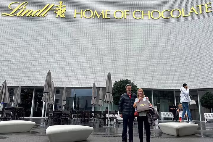 Visitors standing in front of the Lindt Home of Chocolate, holding a bag of chocolates in Zurich.