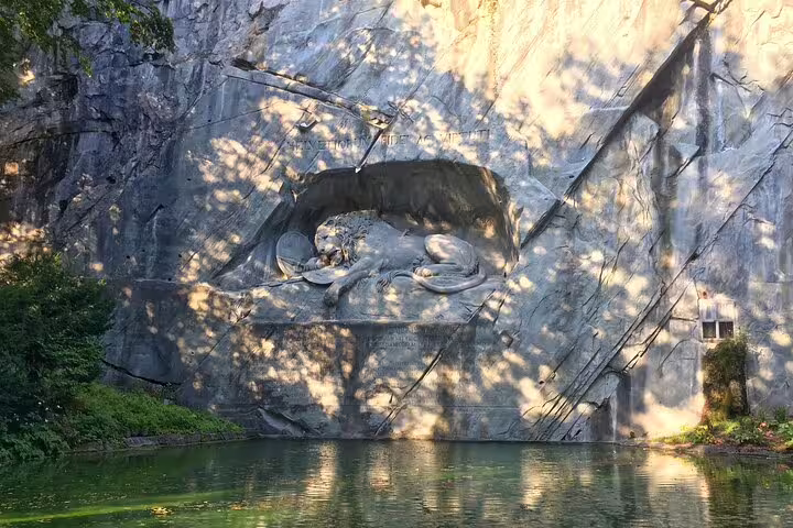 The Lion Monument in Lucerne, carved into rock, reflecting in a tranquil pond on the Zurich small group tour.